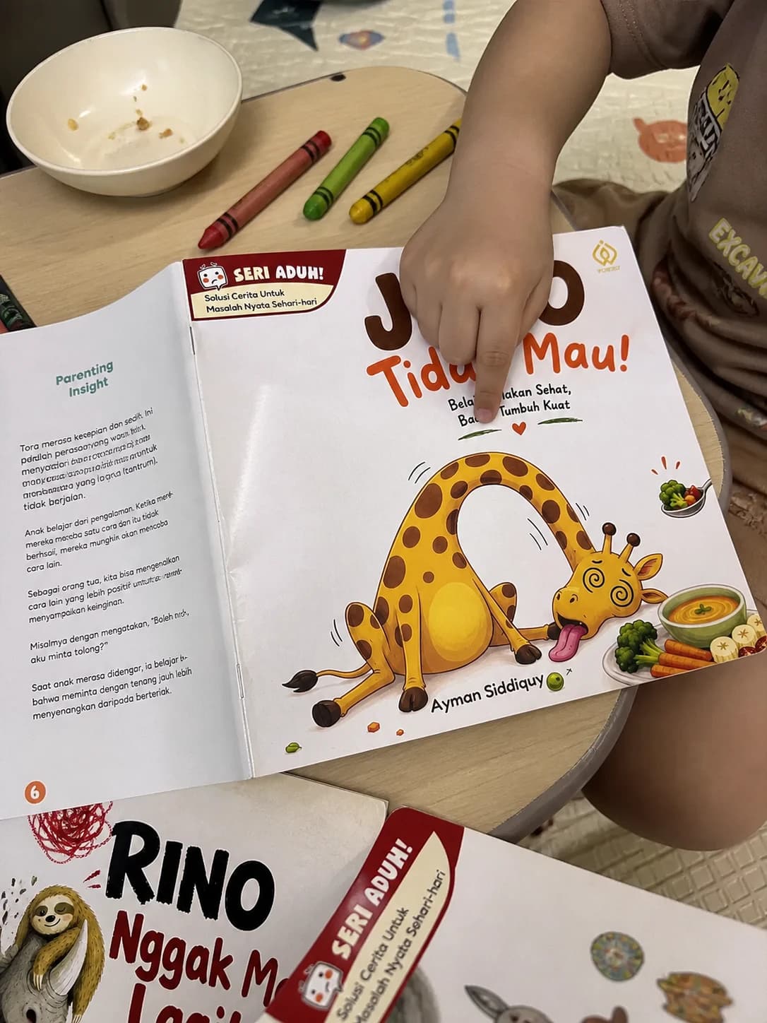 Anak menunjuk buku Jojo Tidak Mau di samping halaman Parenting Insight